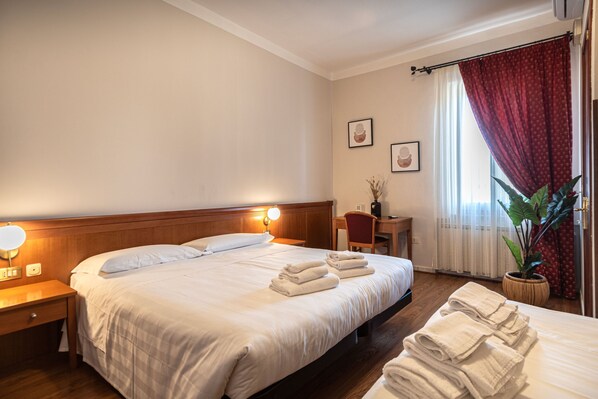 A hotel room with a large bed, bedside tables with lamps, a desk, a chair, a potted plant, and a window with curtains. - Sottoassisi Guest House (Assisi)