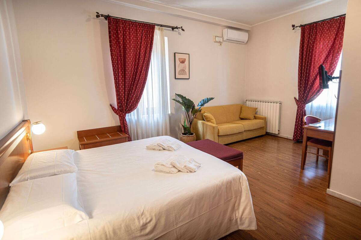A hotel room with a bed, a sofa, a table, and a plant.