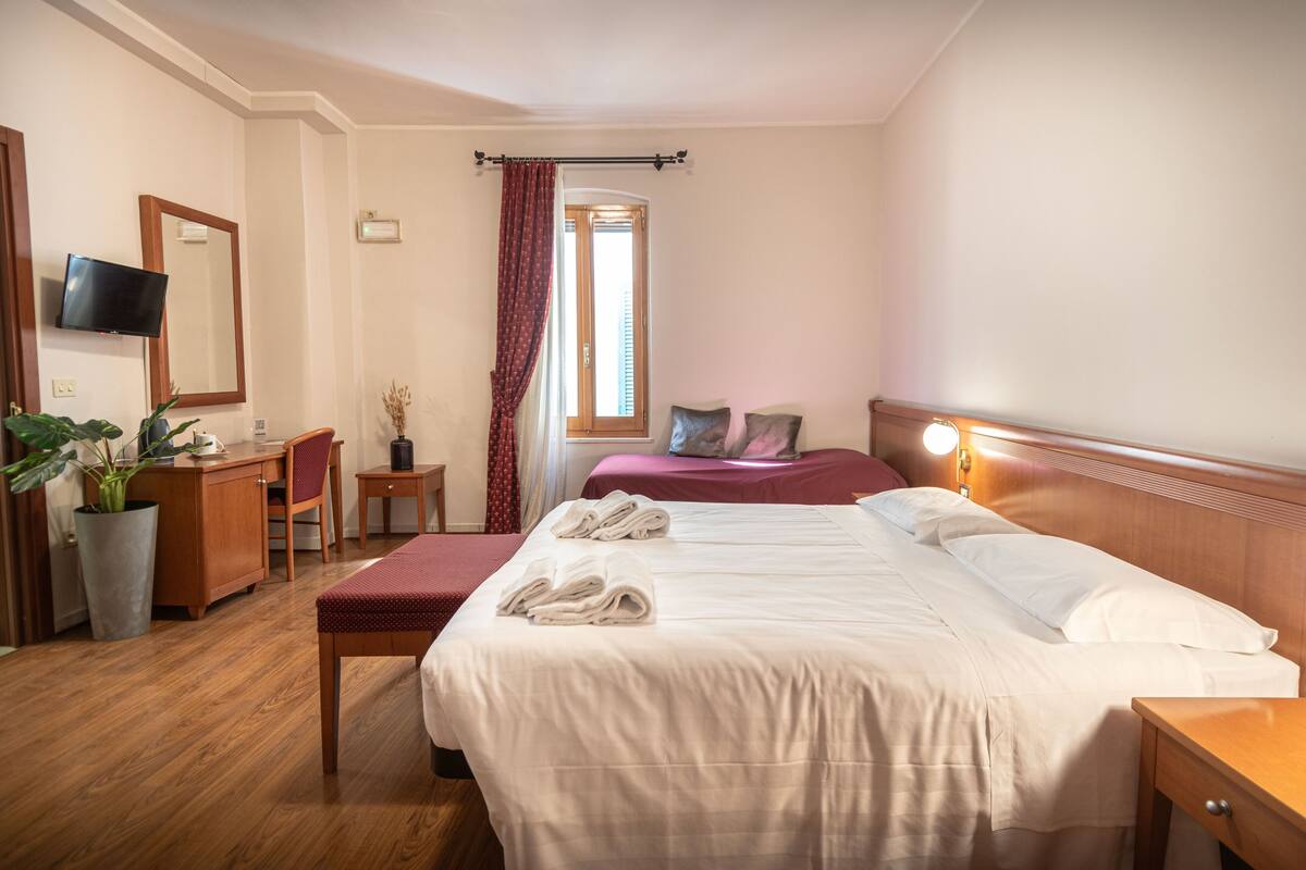 A hotel room with a bed, a desk, a chair, a TV, and a window with curtains.
