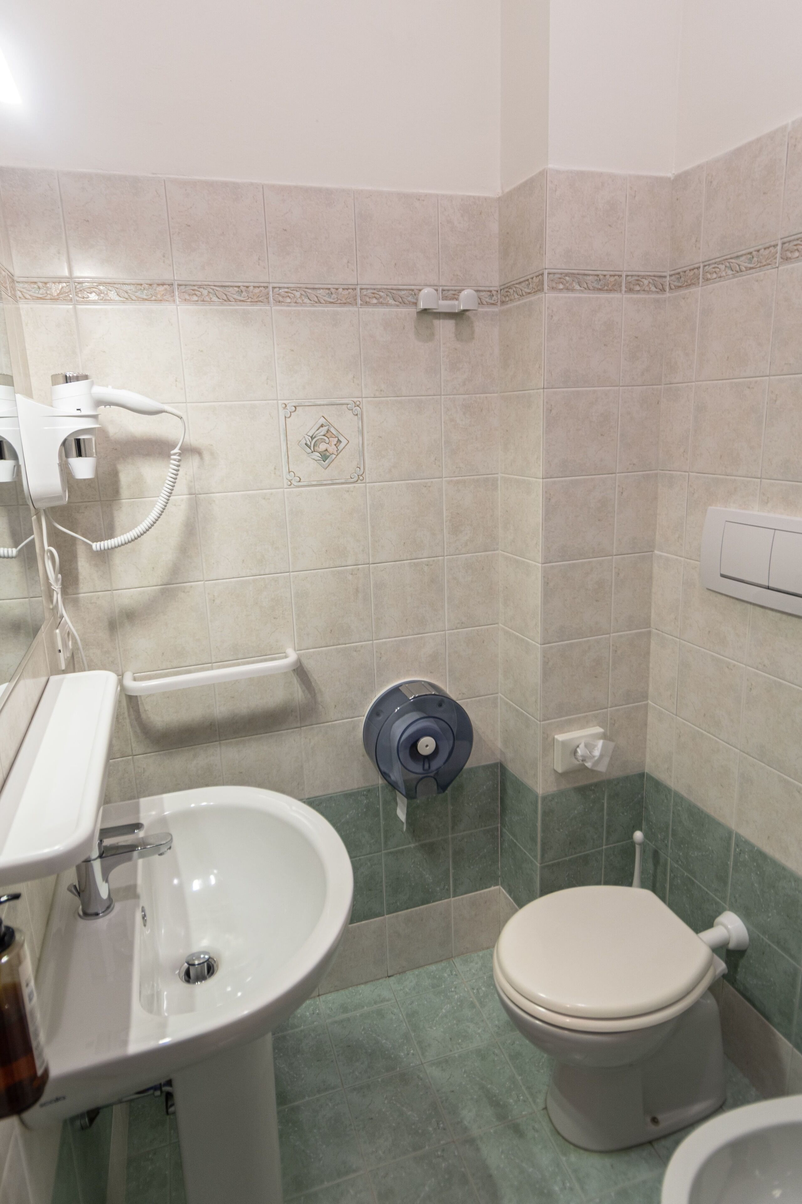 A bathroom with a sink, toilet, and a hairdryer on the wall.