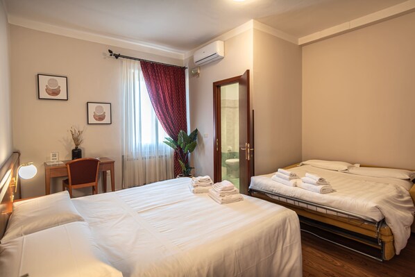 A hotel room with two beds, a desk, a chair, and a bathroom visible through an open door. - Sottoassisi Guest House (Assisi)