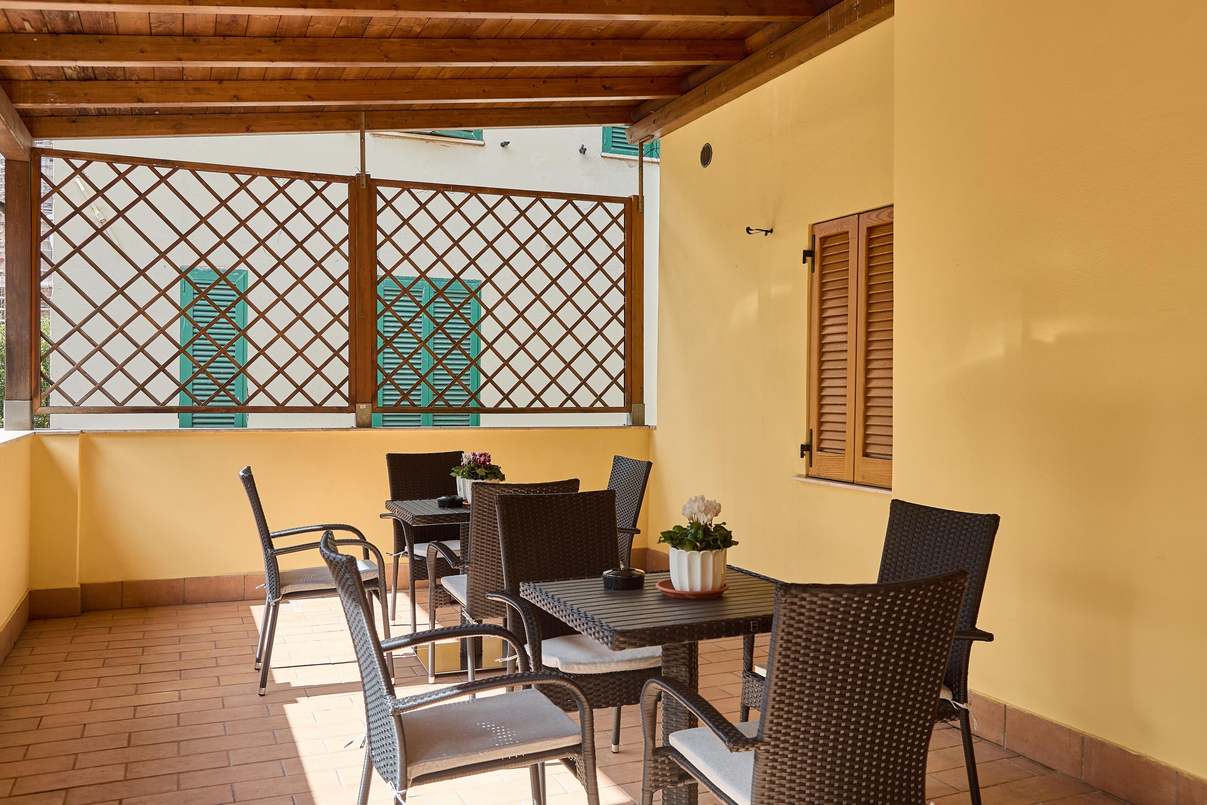Une terrasse avec des meubles en osier, une plante en pot et une vue à travers une fenêtre à treillis.