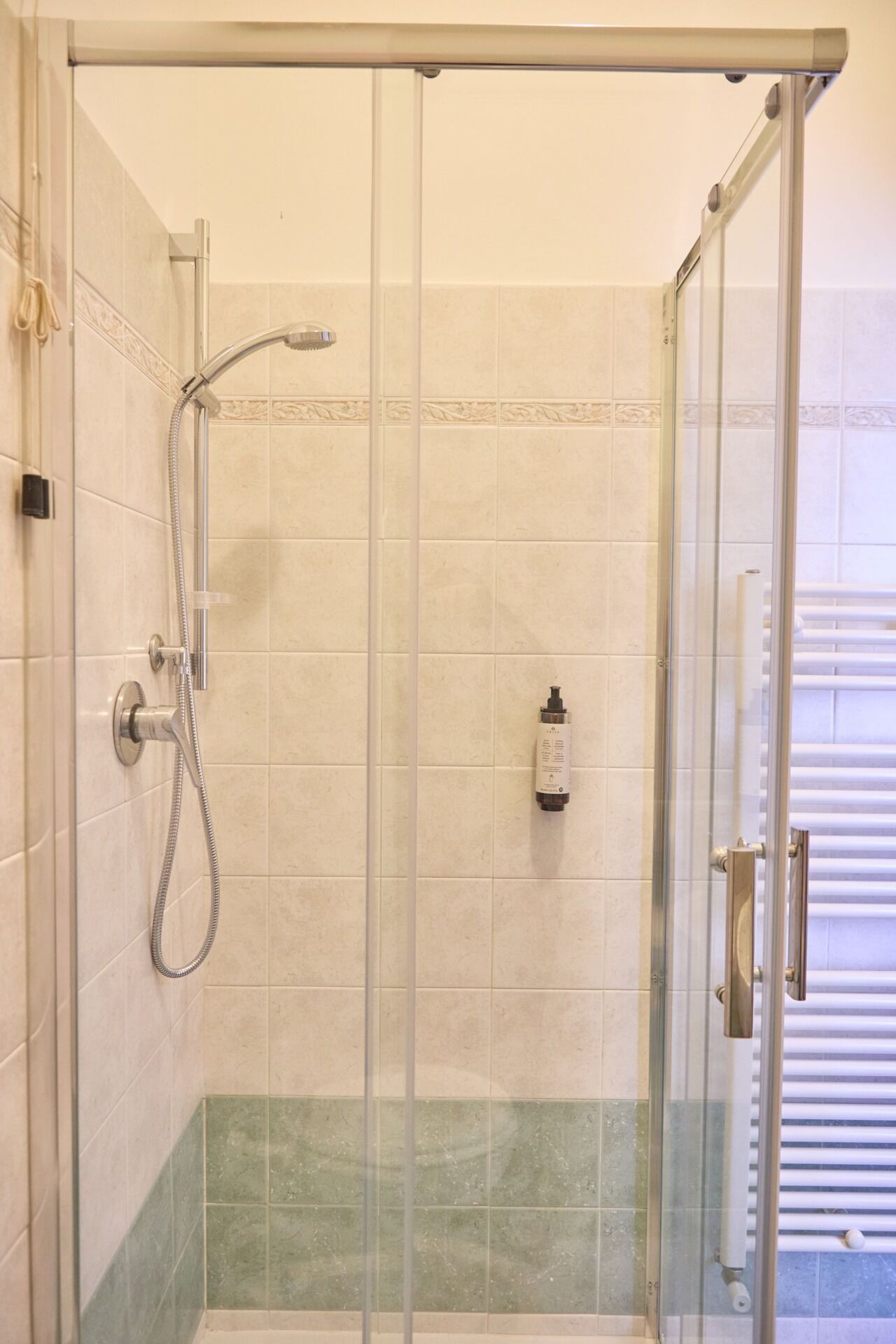 A glass-enclosed shower with a handheld showerhead and a wall-mounted faucet.