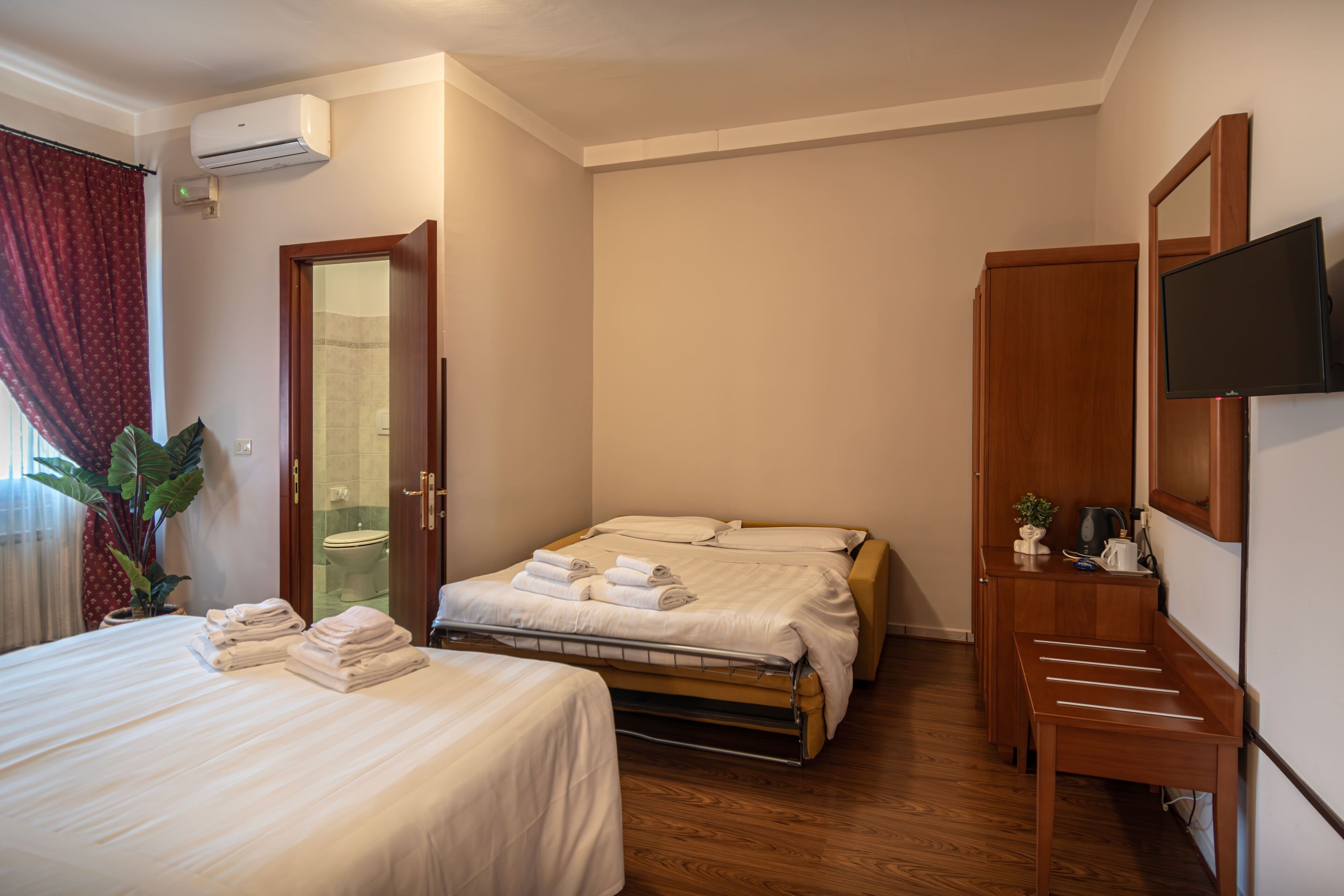 Ein Hotelzimmer mit Bett, Schreibtisch, Fernseher und einem durch eine offene Tür einsehbarer Badezimmer.