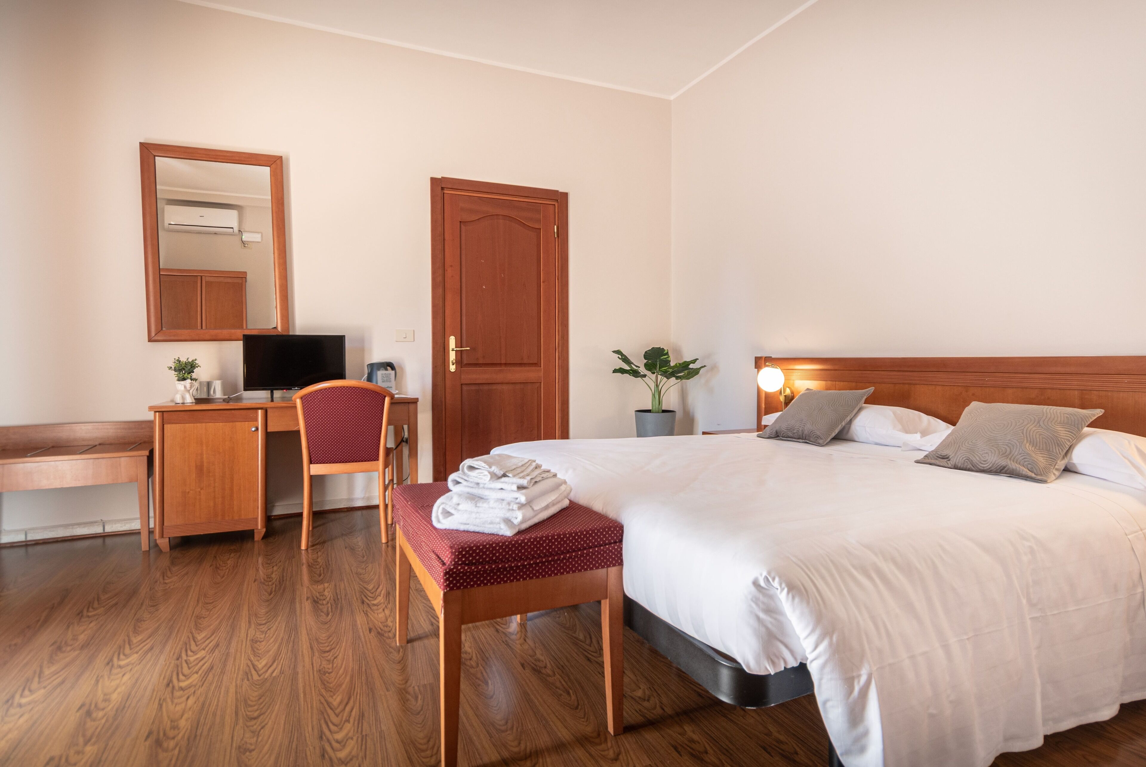 Une chambre d’hôtel avec un bureau en bois, une chaise et un lit recouvert de draps blancs.
