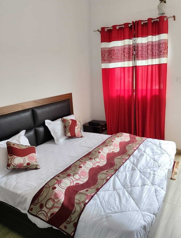 Una cama con una colcha blanca y roja estampada, un cabecero negro y dos almohadas con diseños rojo y blanco.