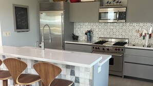 A modern kitchen with a central island, bar stools, stainless steel appliances, and a decorative backsplash.