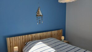 A bedroom with a wooden headboard, a striped bedspread, two bedside lamps, and a wall hanging. - Gite in the heart of Senneville (Senneville-sur-Fécamp)