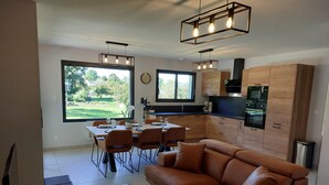 A modern kitchen with wooden cabinets and a built-in oven. There is a dining area with a table set for four and a brown leather sofa. - Gite in the heart of Senneville (Senneville-sur-Fécamp)