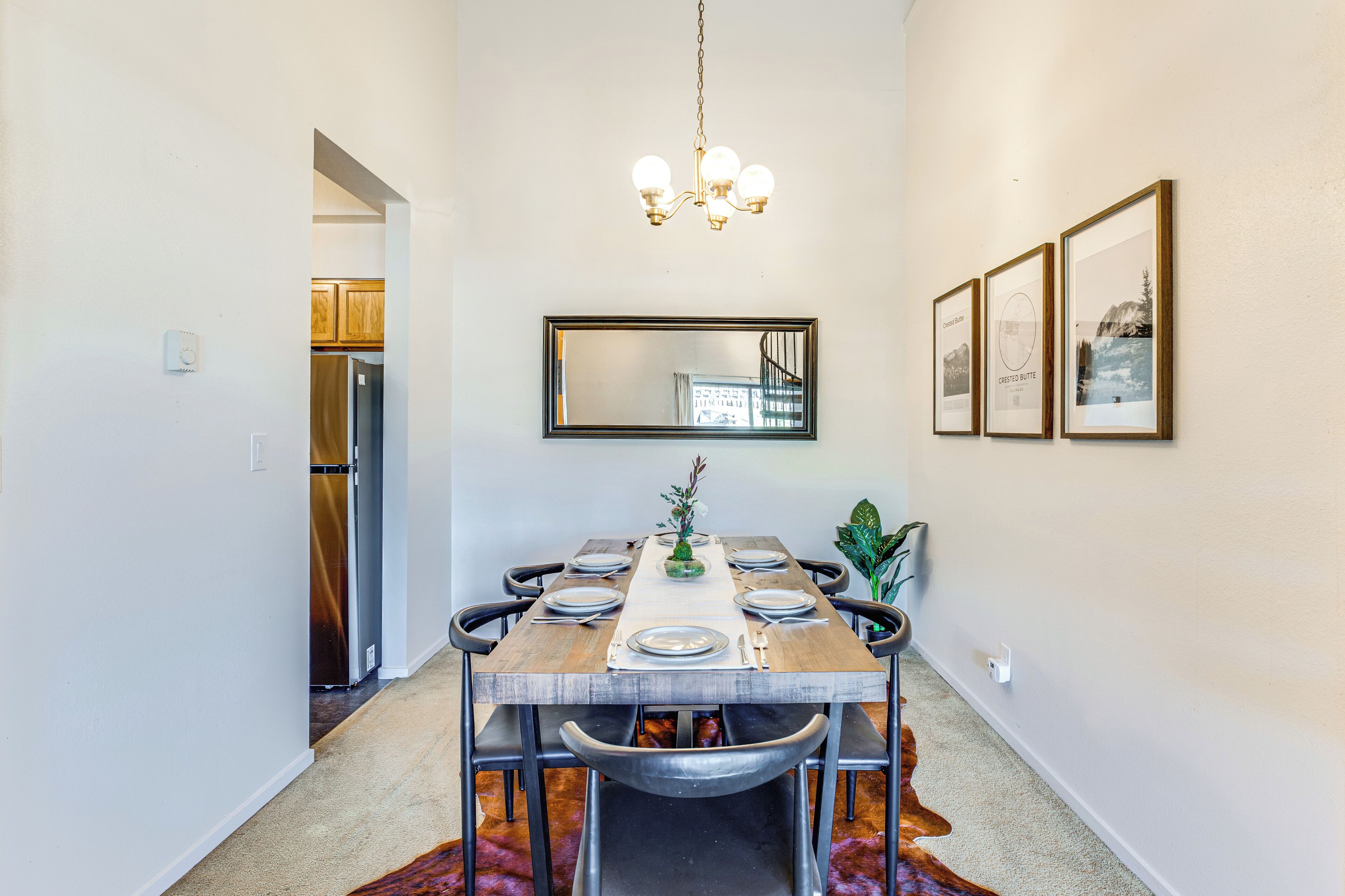 A dining room with a wooden table set for six, a chandelier, a mirror, and framed pictures on the wall.