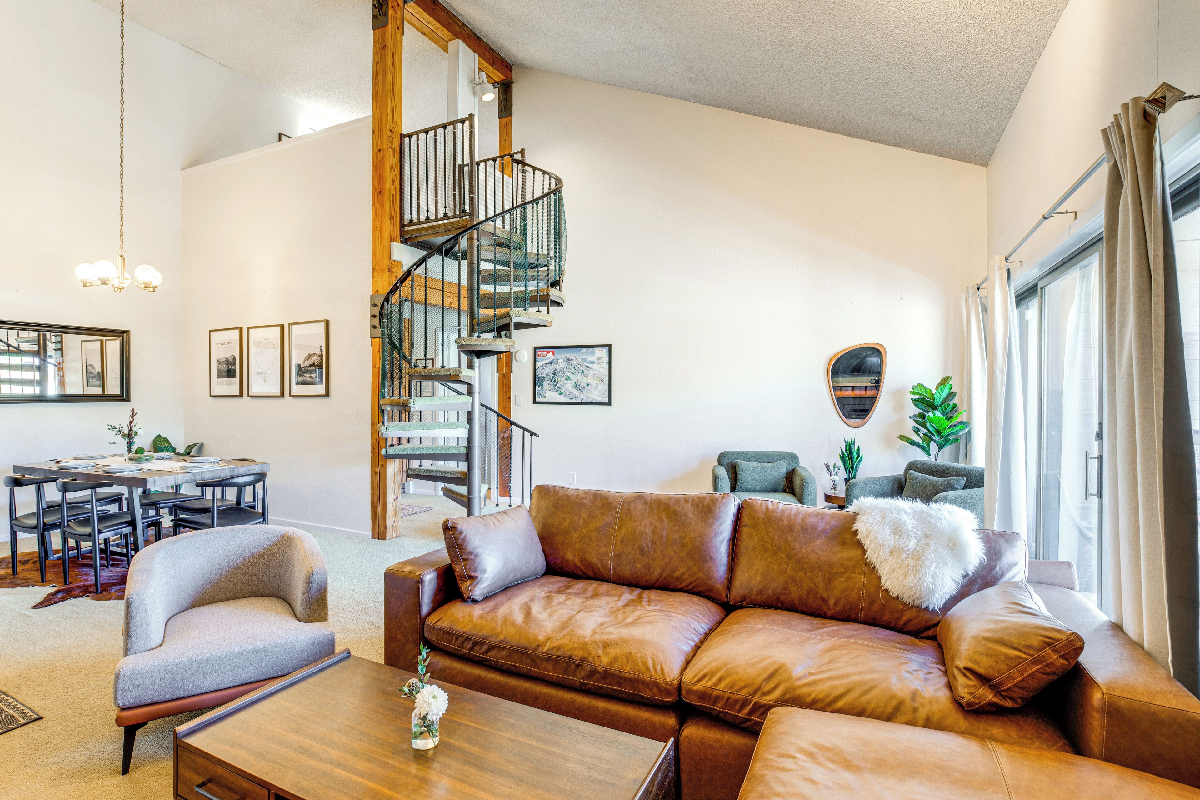 A spacious living room with a brown leather sofa, a wooden coffee table, and a staircase leading to an upper floor.