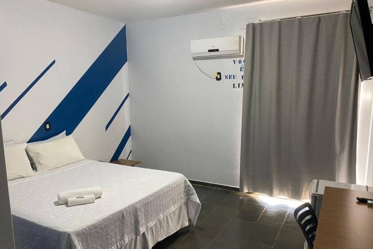 A hotel room with a bed, a desk, a chair, a curtain, and an air conditioning unit.