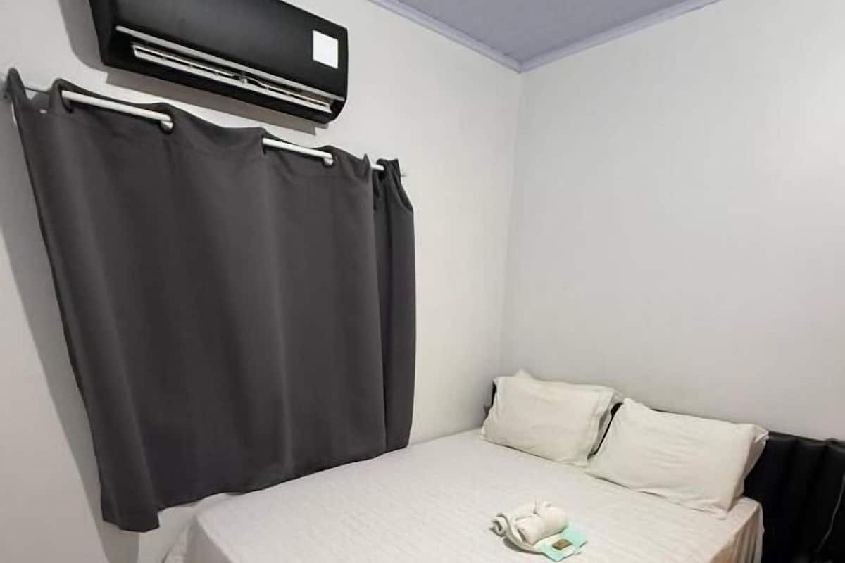 A bedroom with a bed, white curtains, a wall-mounted air conditioner, and a tiled floor.