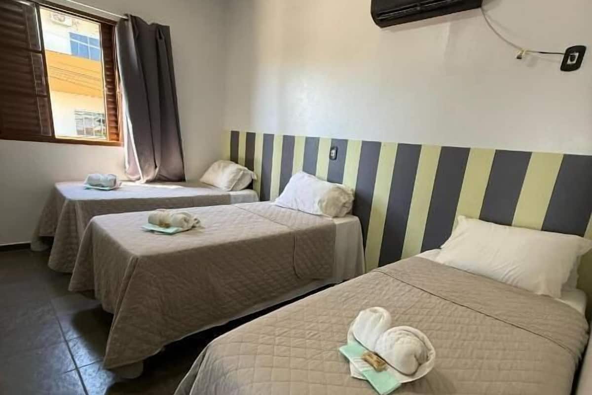 A hotel room with two beds, a window with curtains, and a wall-mounted air conditioning unit.