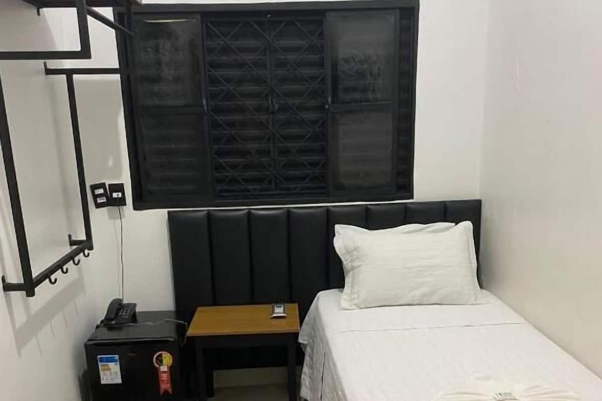 A hotel room with a bed, a bedside table, a nightstand, a telephone, and a wall-mounted air conditioner.