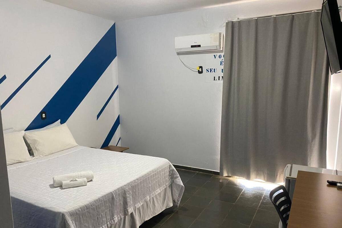 A hotel room with a bed, a desk, a chair, a TV, and an air conditioning unit.