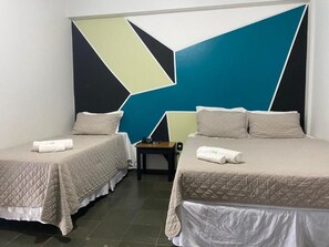 A hotel room with two beds, each with a quilted bedspread and pillows, a small table with a chair, and a geometric wall design. - Hotel Avenida Plaza (Querencia)