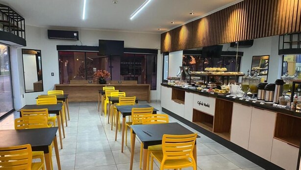 Un área de comedor con sillas amarillas y mesas negras, un mostrador de buffet con diferentes alimentos, y una escalera que conduce a un nivel superior.