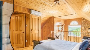 Une pièce de cabane en bois comprenant un lit, un mur en pierre et une fenêtre donnant sur un paysage verdoyant.