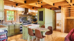 Une cuisine rustique avec un grand poêle, des poutres en bois au plafond et un coin repas comprenant une table et des chaises recouvertes de carreaux.