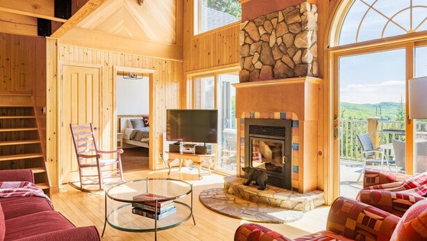 L’intérieur chaleureux d’un chalet avec une cheminée en pierre, des murs en bois, un téléviseur et un coin salon confortable.