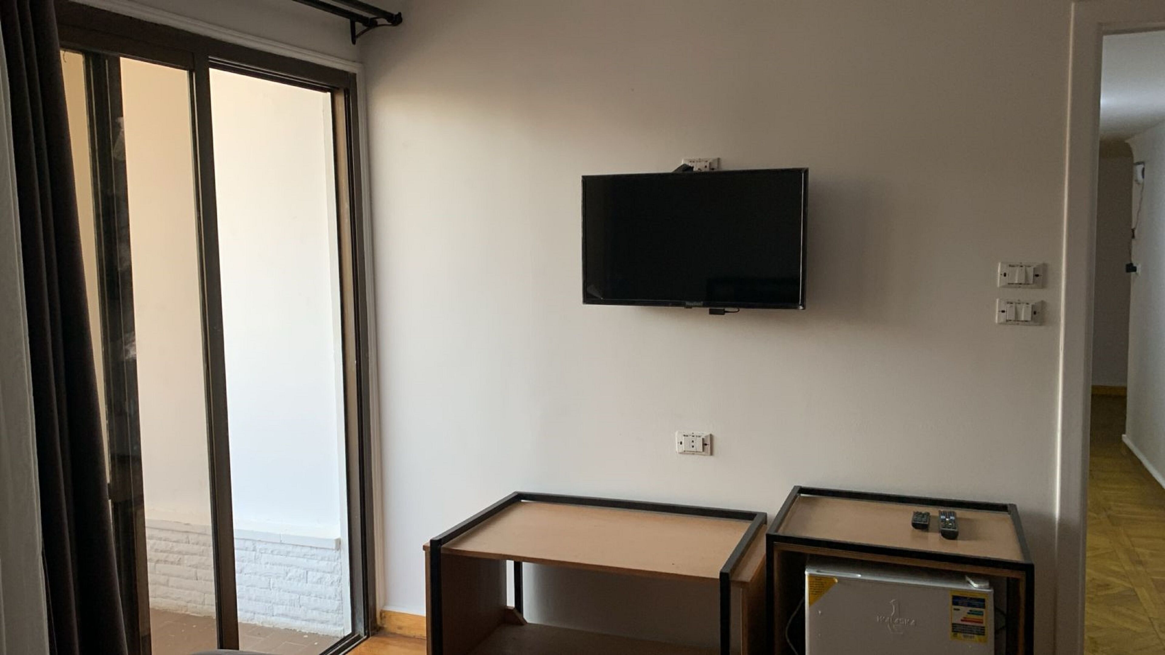 A room with a TV mounted on the wall, a small desk, and a refrigerator.