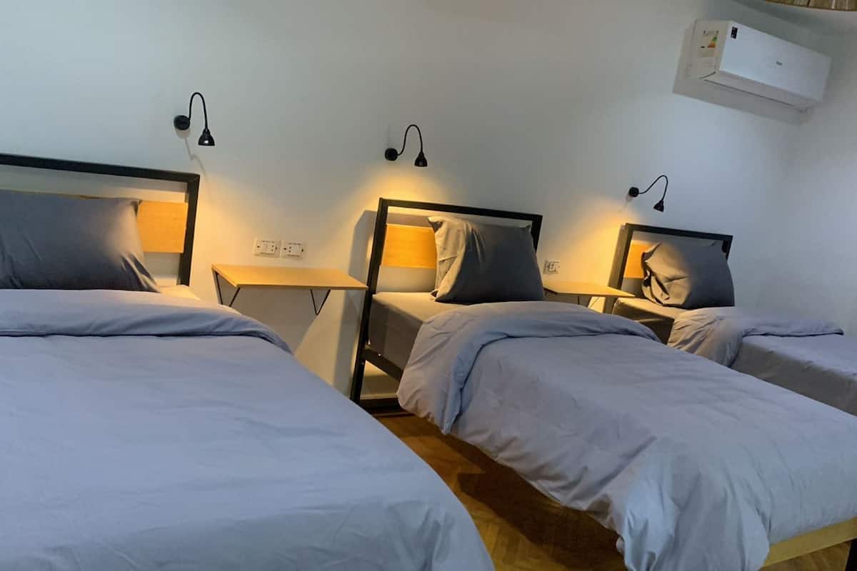 Una habitación con dos camas individuales, cada una con una mesita de noche y lámpara. Hay una pequeña mesa entre las camas, y un equipo de aire acondicionado en la pared.