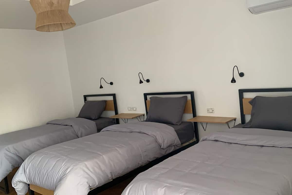 Una habitación con tres camas individuales, cada una con cabecera de madera y una mesita de noche pequeña.
