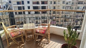 A balcony with wicker furniture, a potted plant, and a view of surrounding buildings. - Pyramids Nights Hostel (Giza)