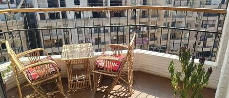 A balcony with wicker furniture, a potted plant, and a view of surrounding buildings.
