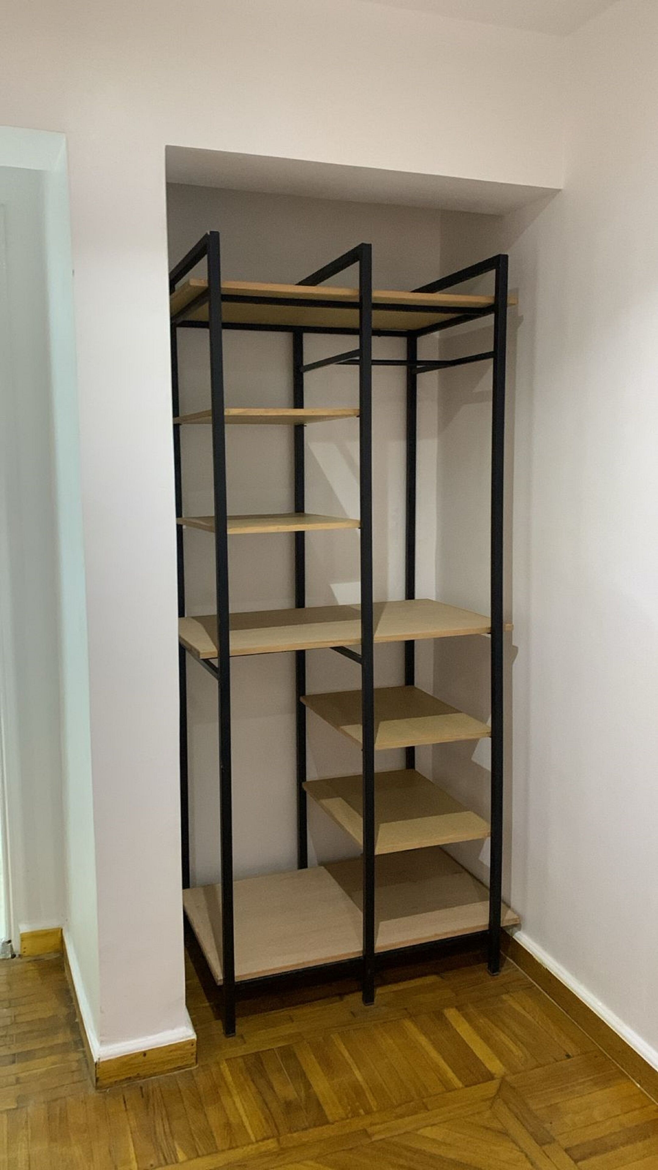 A corner wardrobe with five shelves and a hanging rod, built into a white wall with a wooden floor.