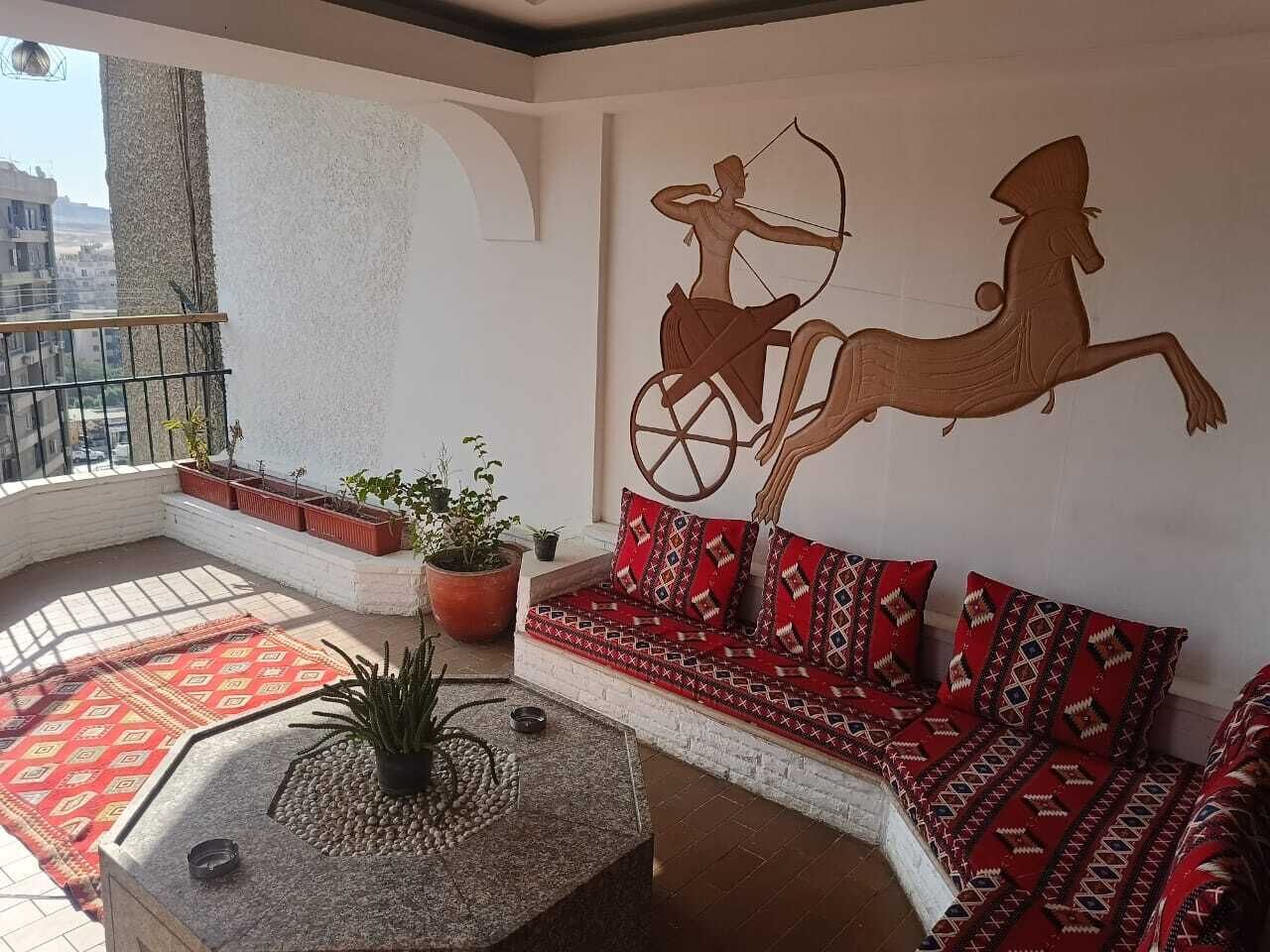 A balcony with a sofa, potted plants, and a decorative wall mural.