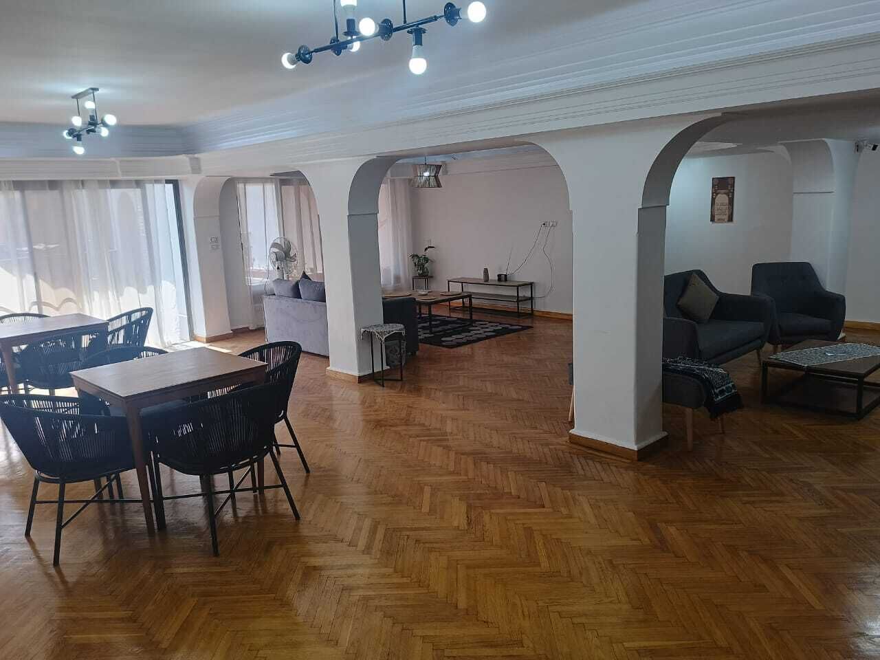 A spacious living area with a wooden herringbone floor, a dining table with chairs, and a sofa set.