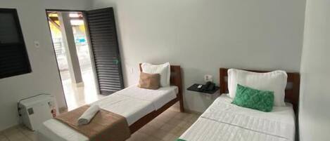 Habitación de hotel con dos camas individuales, una mesita, un buró y aire acondicionado instalado en la pared.