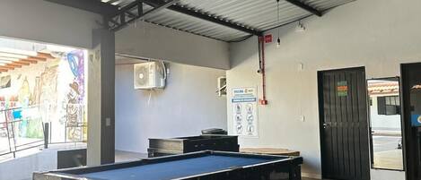 Zona de billar interior con techo metálico, sistema de ventilación y puerta que da al exterior.