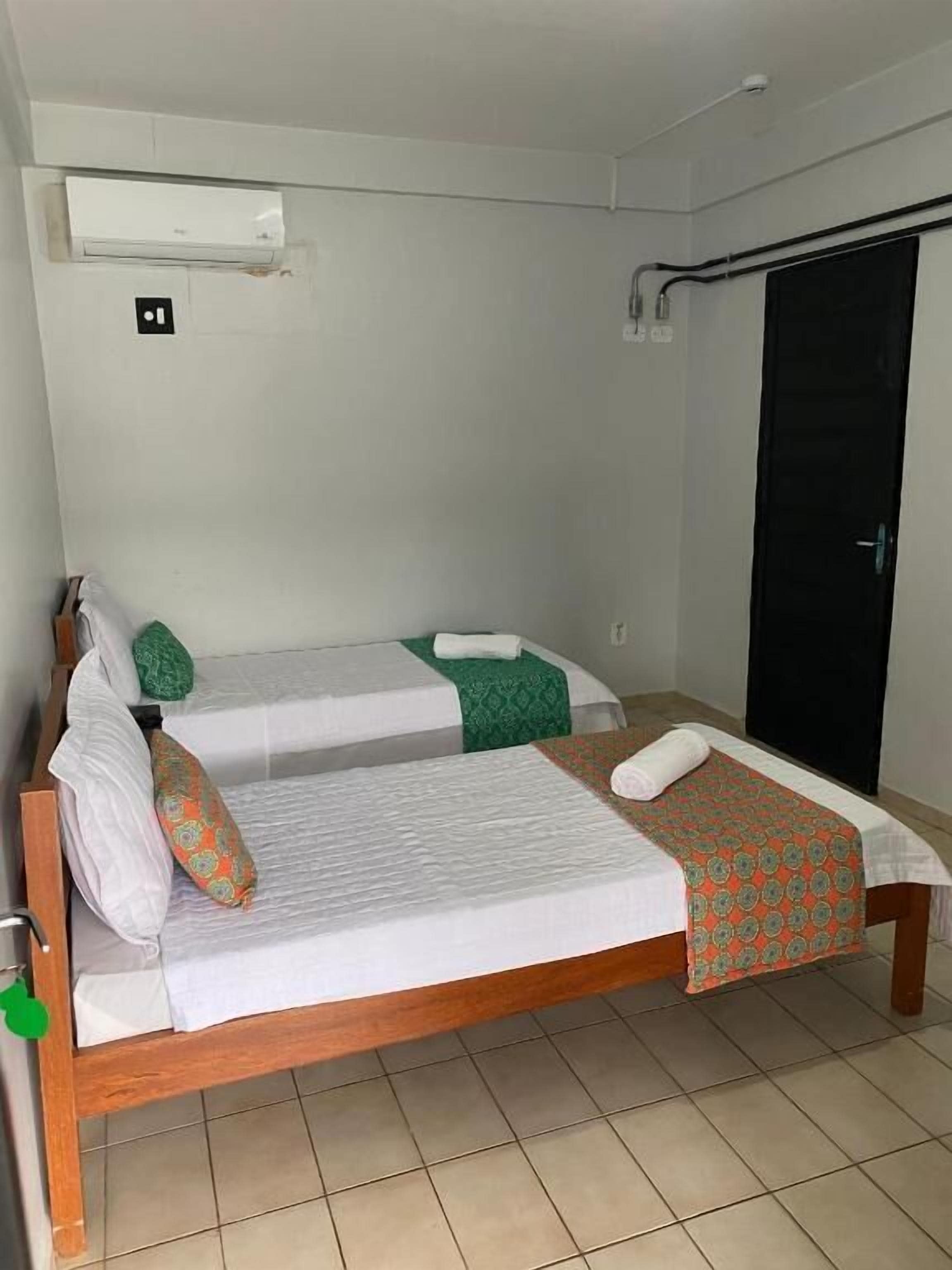 A single bed with a wooden frame, a green and white bedspread, and a white pillow.