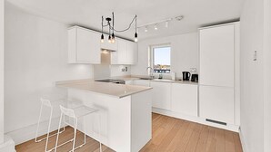 Une cuisine moderne avec des meubles blancs, un îlot central doté de tabourets de bar et une vue par la fenêtre.
