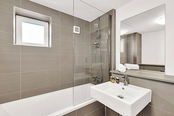 A modern bathroom with a bathtub, a sink, a shower, and a large mirror.