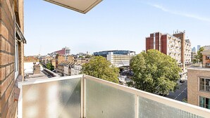 Un immeuble de grande hauteur, avec de nombreux étages, un ciel dégagé et une rue bordée d’arbres au premier plan.
