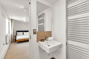 A hotel room with a bed, a white sink, and a mirror. - 2-Bed, 2-Bath Third Floor Flat (London)