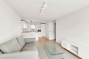 Un espacio moderno con sofá, una mesita de vidrio y una cocina al fondo.