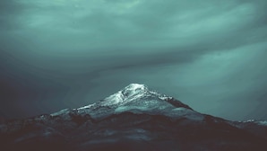 A mountain with a snow-capped peak under a cloudy sky.