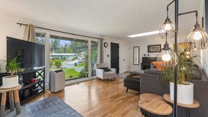 A modern living room with a large TV, comfortable seating, a fireplace, and a view of the outdoors.