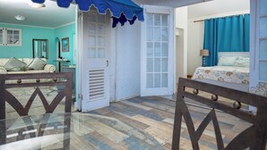 A room with a teal color scheme, a bed with a patterned bedspread, a window with blue curtains, and a door with a white frame. - LillyBelleMar,San San Port Antonio,with pristine views and world class amenities (Fairy Hill)