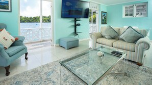 A living room with a large TV, a sofa, a coffee table, and a view of the sea through the glass door. - LillyBelleMar,San San Port Antonio,with pristine views and world class amenities (Fairy Hill)