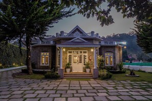 A stone building with a symmetrical facade, a central entrance with steps, and a small porch area. - Savithri  Bungalow By XploreIndo (Kodaikanal)
