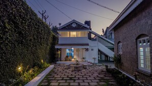 Una casa de dos plantas con un patio, un espacio de estar cubierto al aire libre y un camino de ladrillo que conduce a la entrada.