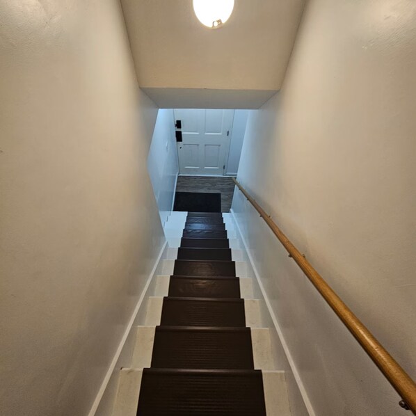 Una escalera con barandal de madera que lleva a una puerta blanca al final.
