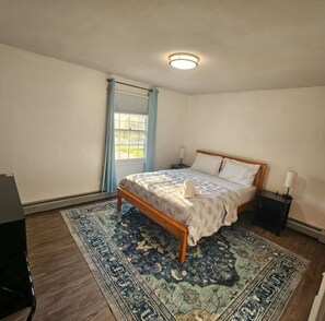 A bedroom with a bed, a nightstand, a lamp, a window with curtains, and a patterned rug.