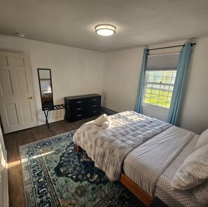 A bedroom with a bed, a dresser, a mirror, a window with curtains, and a patterned rug. - 2 bedrooms that are warm and comfortable queen size beds

 (Williston)